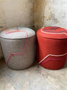 2 footstools in the corner of a faded empty room, one is grey, one is orange